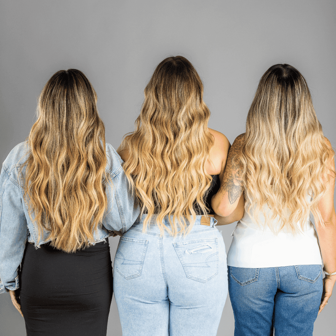 Three women with long, wavy blonde hair standing with their backs facing the camera.
